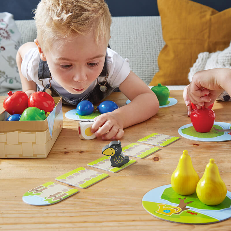 Boy leaning down to pick up a die from HABA First Orchard game